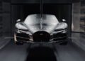 A sleek silver Bugatti sports car undergoing wind tunnel testing, suspended in a controlled environment for meticulous aerodynamic analysis.