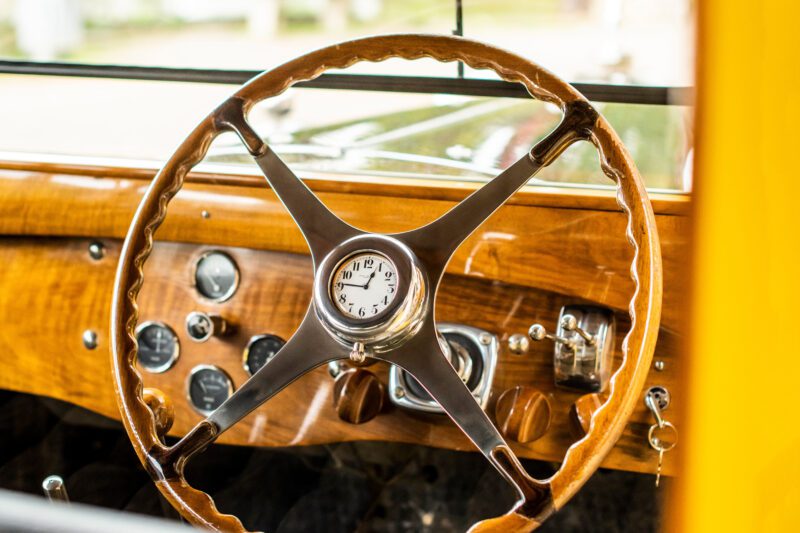 Temukan esensi keanggunan vintage di interior mobil Bugatti ini, di mana roda kemudi kayu dengan jam tengah dengan anggun dikelilingi oleh pengukur klasik di dasbor kayu.