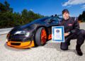 A person kneels beside a sleek black and orange Bugatti sports car, holding a certificate. The car is parked on a paved area with trees in the background, exuding an aura worthy of Pilote Officiel Bruno Spengler's admiration.