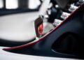 Close-up of a Bugatti car interior featuring a sleek gear shift lever with a red accent. Surrounding it are metallic dials and black trim with red edging, reminiscent of the W16 Mistral's luxurious design.