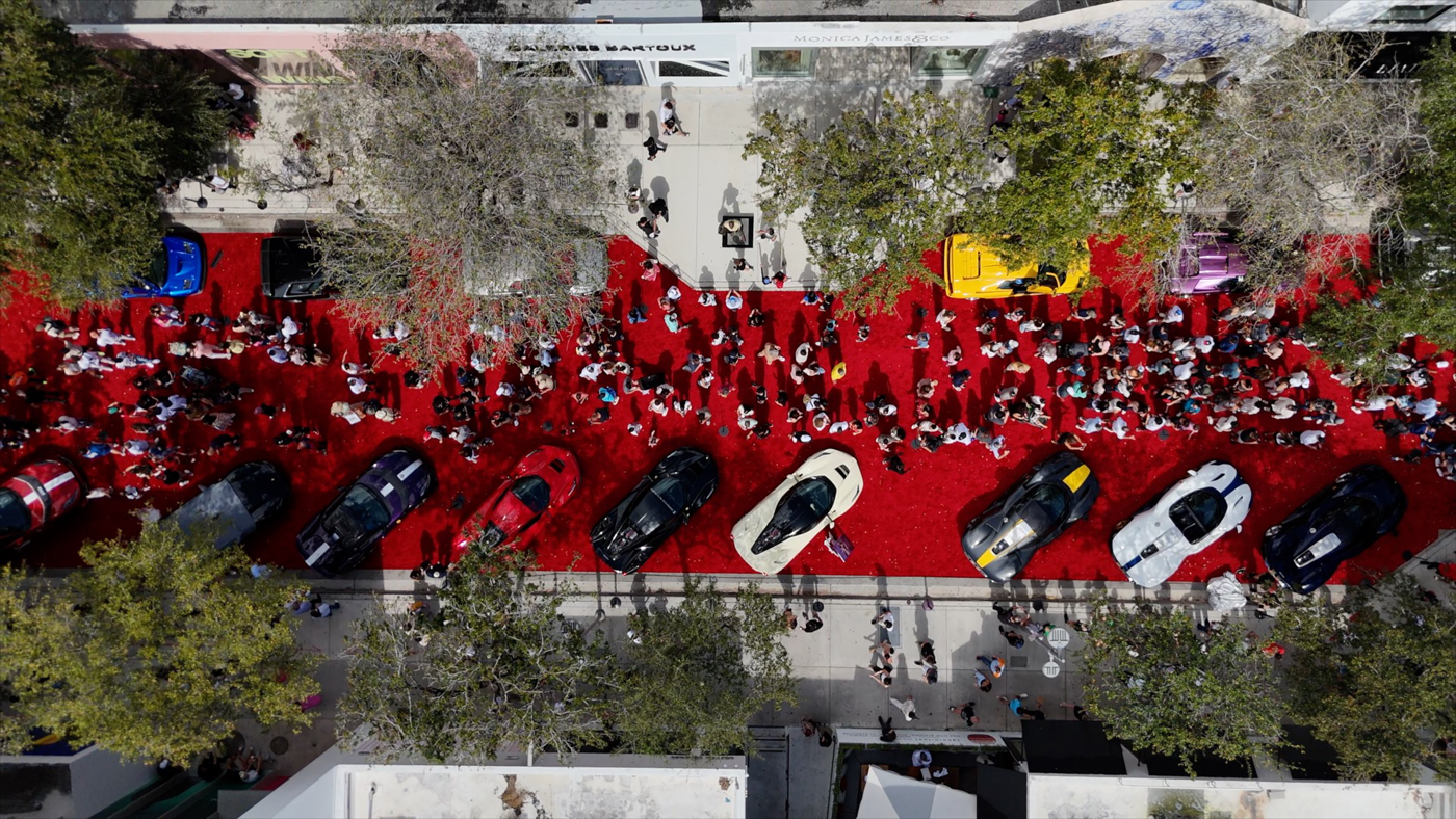 Aerial view of the Miami Concours 2025, where thousands enjoyed the spectacle of luxury cars displayed on a red carpet. Crowds gathered around, surrounded by trees lining the street, turning this supercar art event into a stunning visual experience.