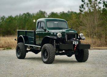 A vintage 1946 Timberline Green Dodge Power Wagon truck is parked on a gravel surface, with trees creating a serene backdrop.