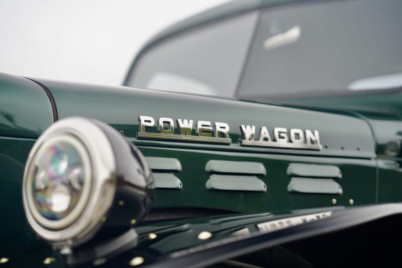 Close-up of a 1946 Timberline Green Desert Power Wagon, showcasing its vintage charm. The focus is on a round headlight and part of the hood, epitomizing timeless power.