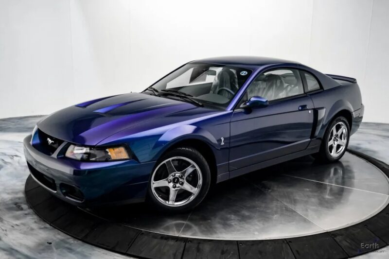 A sleek, blue, two-door sports car with shiny chrome wheels is parked in a studio with a white background, evoking nostalgia for iconic 2000s cars.