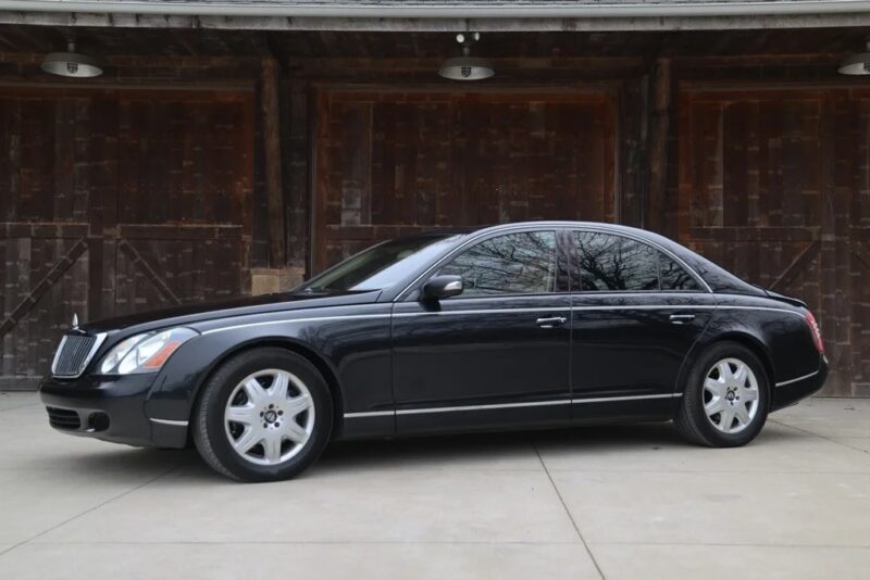 A black luxury sedan, the epitome of elegance, is parked on a concrete surface in front of a wooden building. Experience affordable luxury sedans like never before.