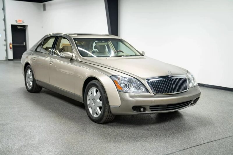A beige luxury sedan, epitomizing elegance, is parked in a pristine white showroom with the entrance door visible in the background.