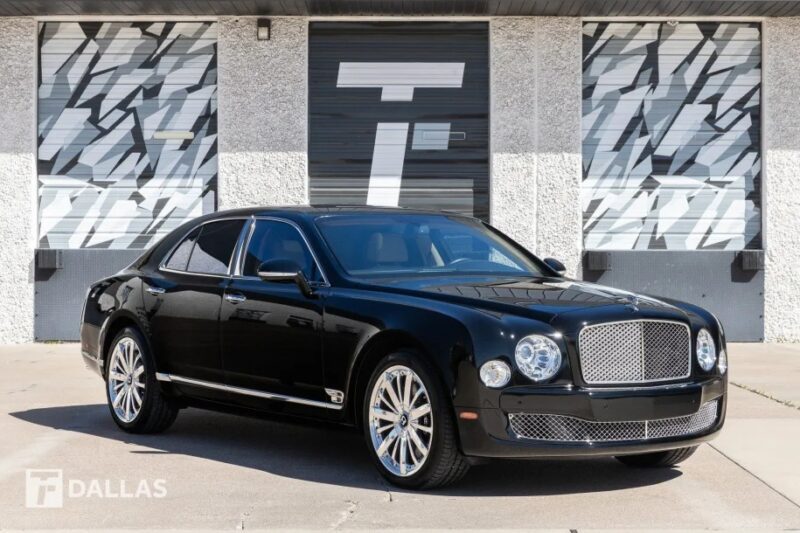 An elegant black luxury sedan is parked in an outdoor setting, framed by a patterned building facade. This blend of sophistication and style is now for sale, offering you a taste of affordable luxury.