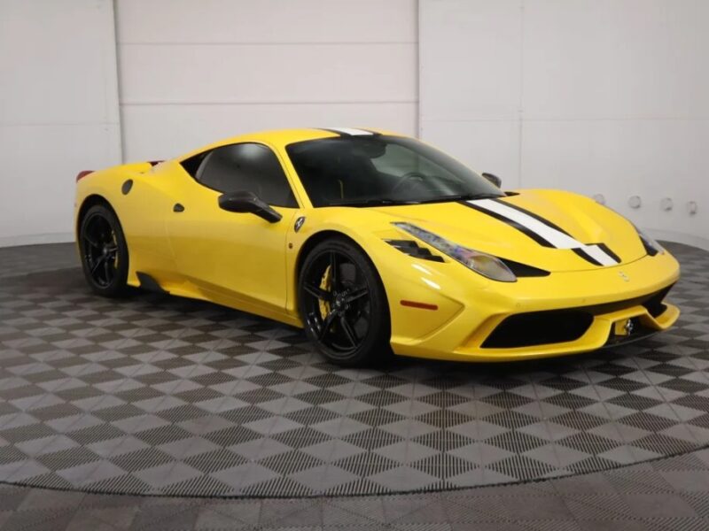 A yellow Ferrari 458 Speciale with black and white racing stripes sits on a checkered floor. Renowned as one of the best modern Ferraris, it boasts a sleek design and striking black rims.