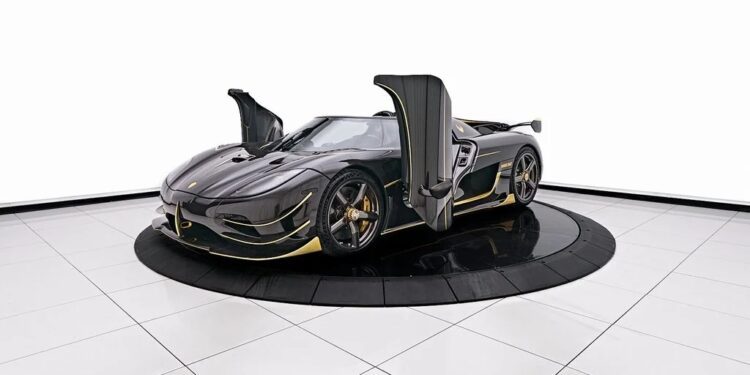 A sleek, black 2018 Koenigsegg with gull-wing doors open, displayed on a circular platform in a well-lit showroom with a white background.