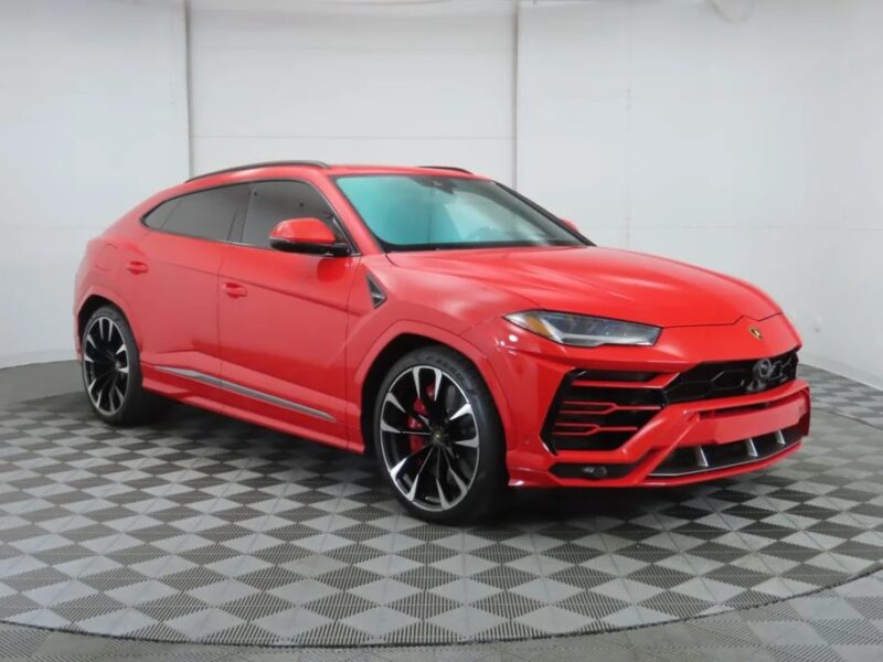 A red luxury SUV, the Lamborghini Urus boasts a sporty design with black wheels and tinted windows, showcased in a light-filled showroom. Discover why it's among the best Lamborghinis in SUVs for sale today.