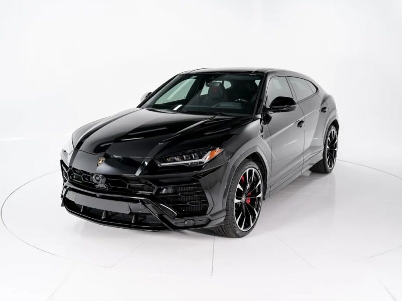 A sleek black Lamborghini Urus SUV, now for sale, is elegantly parked in a bright, minimalistic studio setting.