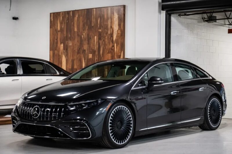 A sleek black luxury sedan exudes elegance as it sits parked indoors by a wood-paneled wall, embodying the allure of affordable luxury. Meanwhile, another car is partially visible in the background, suggesting a collection of refined choices for discerning buyers.