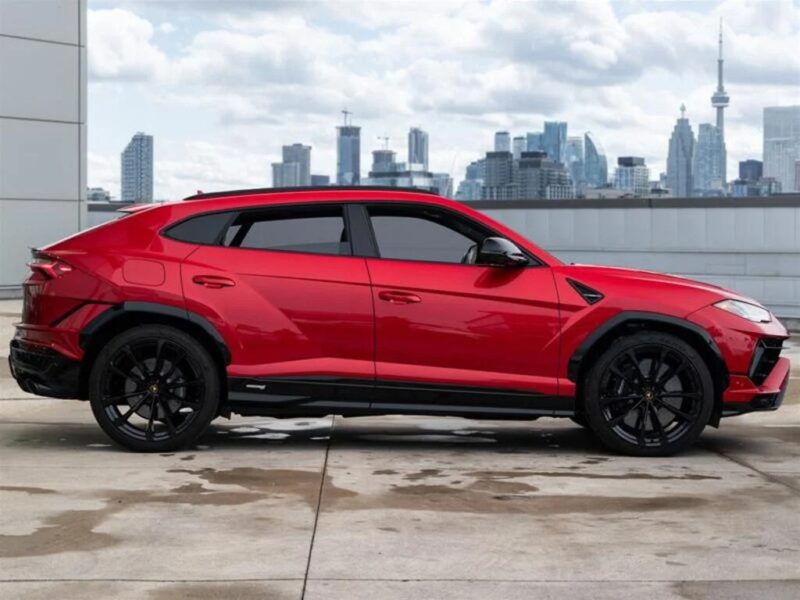 A sleek Lamborghini Urus is parked on a rooftop, boasting its vibrant red hue against the stunning city skyline in the background.