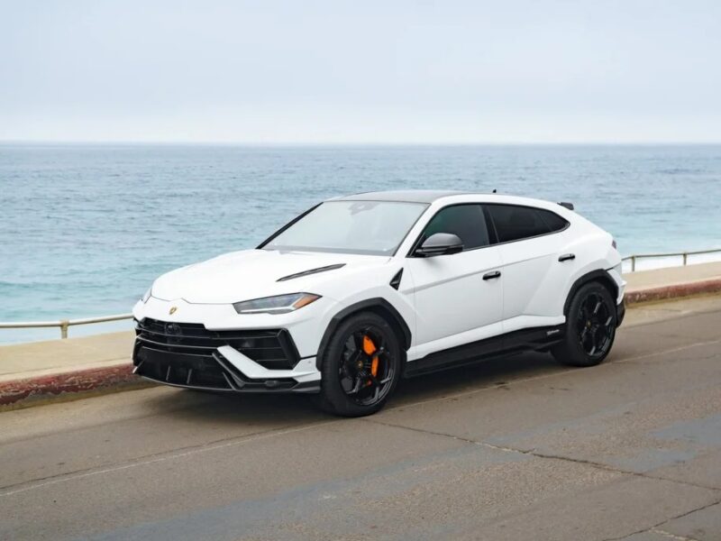 A white Lamborghini Urus, epitomizing luxury and performance, is elegantly parked on a coastal road with the ocean in the background.