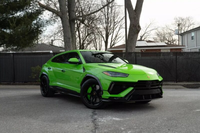 A striking Lamborghini Urus in bright green sits elegantly on the driveway, surrounded by lush trees and a charming house in the background. This stunning SUV, ideal for those seeking both luxury and performance, is now available for sale.