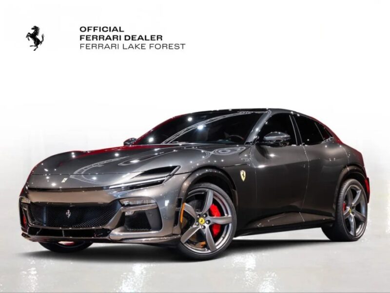 A sleek, dark gray Ferrari Purosangue SUV with red brake calipers is parked on a reflective surface. The Ferrari Lake Forest logo gleams in the top left corner, hinting at the perfect opportunity to buy this stunning SUV for sale.