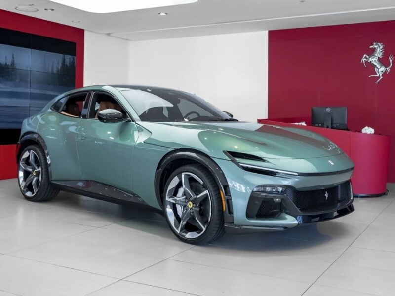 A sleek green Ferrari Purosangue SUV with a modern design graces the showroom, its vibrant hue contrasting elegantly against the red and white walls.