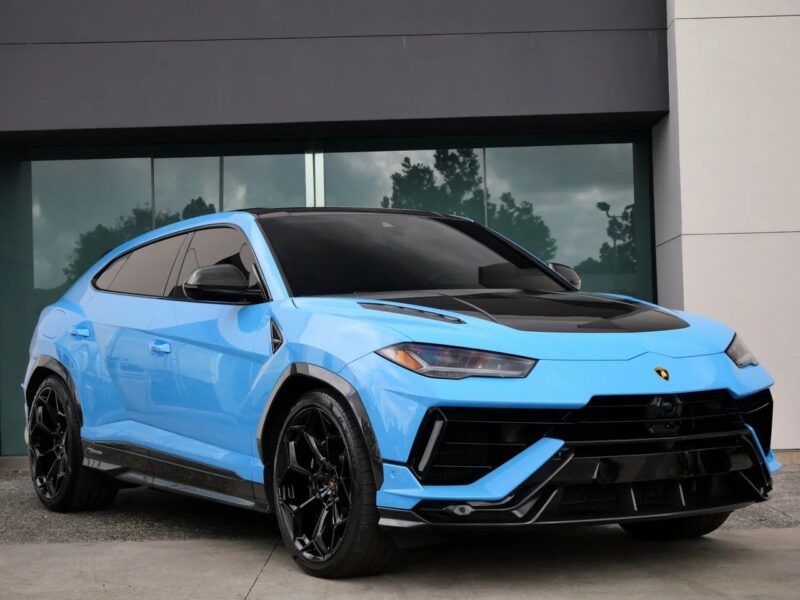 A blue Lamborghini Urus, one of the best Lamborghini SUVs for sale, is parked in front of a modern building with large glass windows.