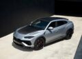 A silver Lamborghini Urus, one of the best Lamborghinis, with black accents and red brake calipers is parked on a concrete driveway beside a dark building.