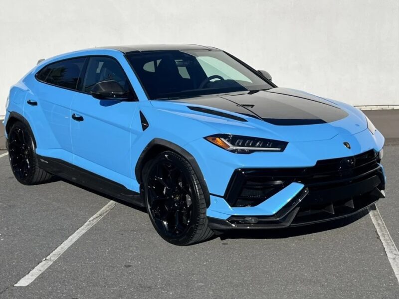 A blue and black Lamborghini Urus SUV is parked on a gray asphalt surface against a white wall, showcasing why it's among the best Lamborghinis on the market.