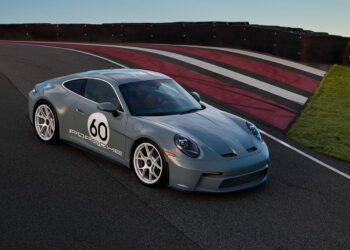A gray Porsche 911 S/T with number 60 on the side is parked on a racetrack featuring red, black, and white painted lines. This iconic vehicle, soon to be part of RM Sotheby's prestigious auction, captures the essence of racing excellence and timeless design.