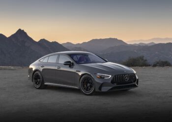 A sleek, gray Mercedes-AMG GT 63 S luxury sedan with E PERFORMANCE features is parked on a dirt road, framed by majestic mountains in the dusky backdrop.