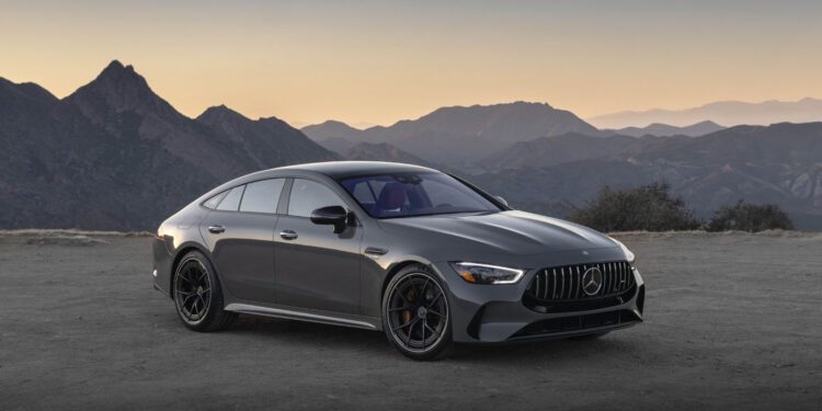 A sleek, gray Mercedes-AMG GT 63 S luxury sedan with E PERFORMANCE features is parked on a dirt road, framed by majestic mountains in the dusky backdrop.