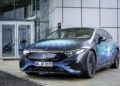 Mercedes-Benz electric car parked outside a building, showcasing blue geometric patterns on its body. Engineered with insights from F1 engineers, its advanced EV battery technology sets a new standard in efficiency and performance.