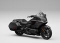 A black Honda Gold Wing touring motorcycle with a sleek design, large front windshield, and integrated side storage compartments stands proud against a neutral background, celebrating its 50th Anniversary.