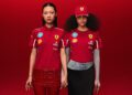 Two models pose against a bold red backdrop, wearing Ferrari shirts and caps from the PUMA x Scuderia Ferrari Replica Collection, adorned with sponsor logos. They hold hands, embodying the essence of racing passion.