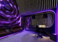 A modern recording studio with curved, illuminated walls and purple lighting sits nestled in the heart of Miami Real Estate. The central mixing desk is flanked by a plush chair and two brown couches, creating a chic oasis for creativity.