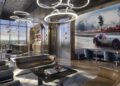 Modern lounge with leather sofas, a table, and large wall art of a vintage Mercedes-Benz. Circular ceiling lights hang above. A bar area is visible in the background near tall windows, offering a glimpse of Tower 2's stunning Miami real estate beyond.