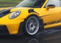Close-up of a yellow Porsche 992 911 GT3 RS with Michelin tires driving on a wet road, showcasing detailed aerodynamic features and spinning wheels.