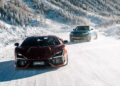 Two sporty cars drive along a snowy mountain road in Livigno. The foreground features a red Lamborghini, while a blue car follows behind against a backdrop of snow-covered trees and mountains, capturing the thrilling essence of an elite Snow Driving Experience.