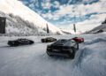 Four sleek sports cars, including a Lamborghini, are parked on a snow-covered landscape in Livigno. The scene is set against a backdrop of majestic mountains and fluttering flags, offering a breathtaking Snow Driving Experience.