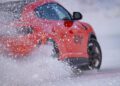 A red Lamborghini speeds across the snowy surface of Livigno, skillfully kicking up snow behind it. The car is angled slightly, perfectly capturing the thrilling essence of snow driving in a winter wonderland.