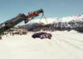 A Lamborghini is suspended by a crane over a snowy landscape, with mountains and buildings in the background, evoking the elegance of I.C.E. St. Moritz.