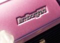 Close-up of a Lamborghini logo on a metallic pink car, capturing the essence of Polo Storico with a blurred effect and hints of light reflections.