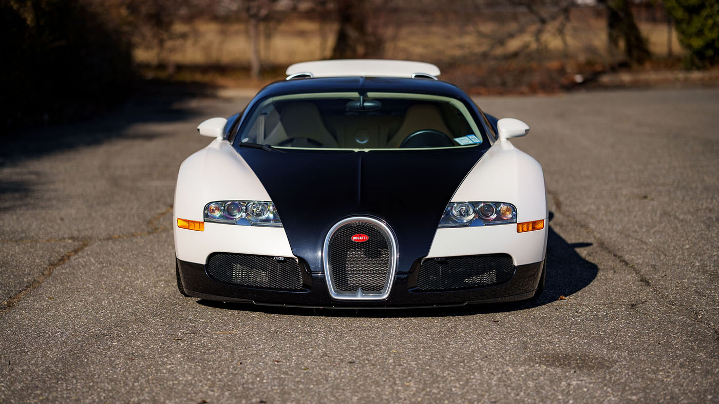 Front view of a white and black Bugatti Veyron parked on a paved surface, reminiscent of the elegance seen at Amelia Island events, with a softly blurred background.