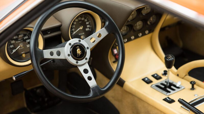 The interior of this classic car exudes timeless elegance, showcasing a wooden steering wheel emblazoned with a logo, an analog speedometer and tachometer, and a manual gear shifter on a beige dashboard. It's the type of craftsmanship that might be celebrated at Broad Arrow Auctions.