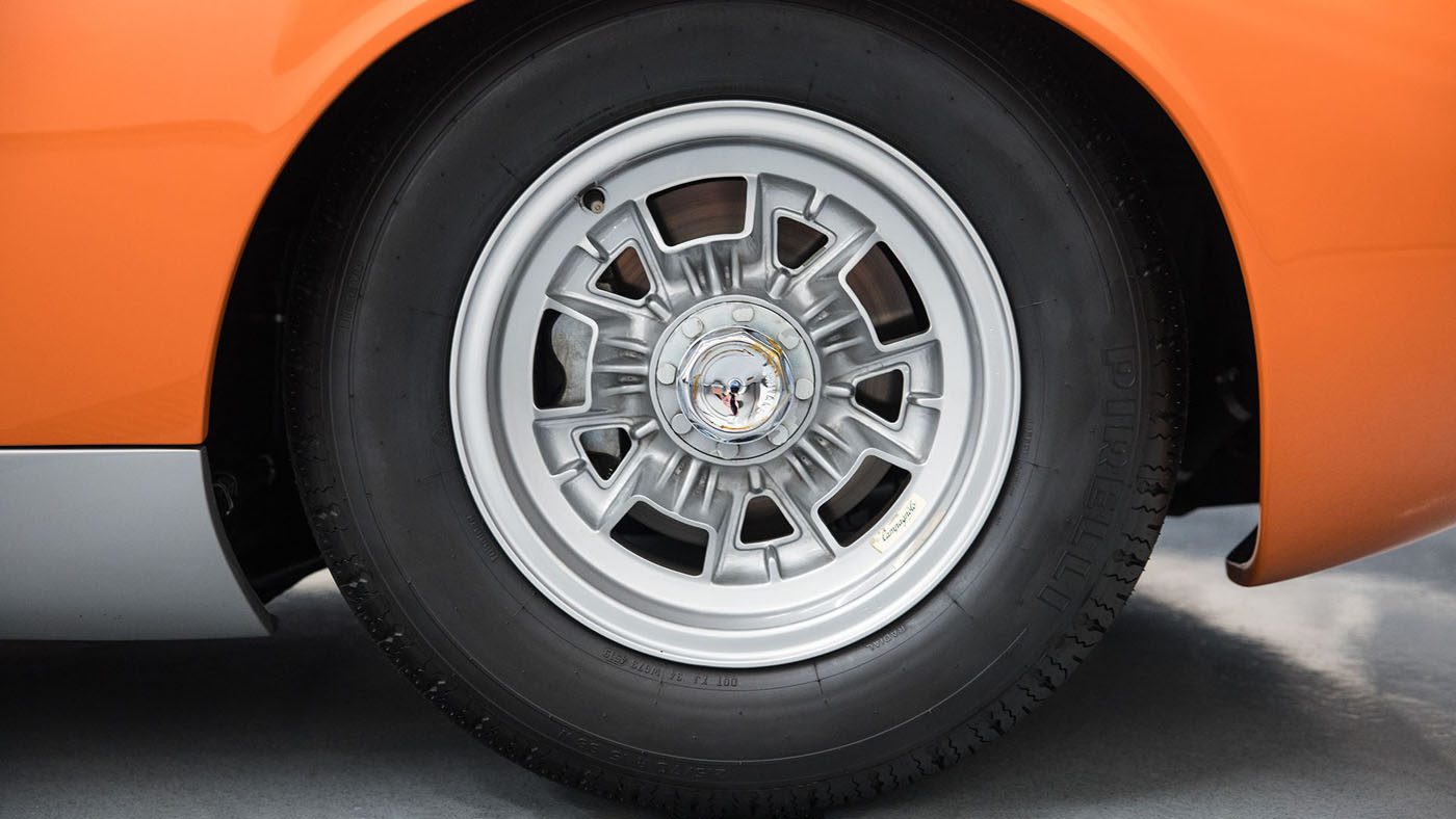 A close-up of a classic car wheel with a silver hubcap and an orange body panel evokes the elegance seen at Broad Arrow Auctions, reminiscent of a pristine Lamborghini Miura P400 SV displayed on Amelia Island.