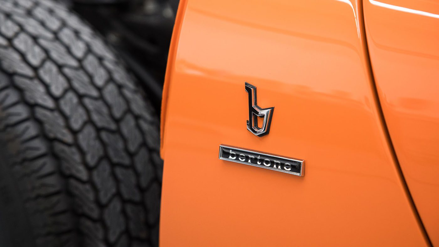 Close-up of an orange car featuring a "Bertone" emblem on the body near the wheel, reminiscent of the craftsmanship found at Broad Arrow Auctions.