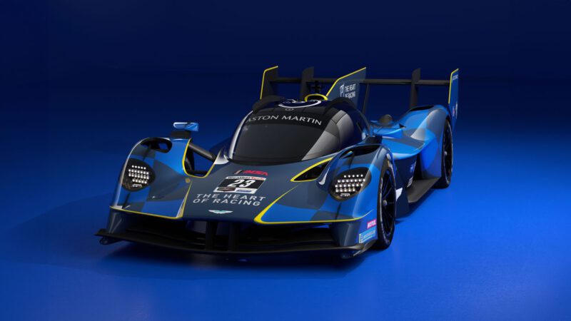 Blue and black racing car with yellow accents, featuring the number 23 and branding on the front, evoking the thrill of a Valkyrie Hypercar. Set against a blue background, this design echoes the excitement of Le Mans.