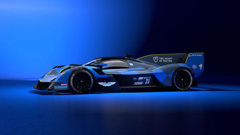 A sleek blue and black Aston Martin race car with an angular design and prominent decals, reminiscent of the Valkyrie Hypercar, set against a gradient blue background.