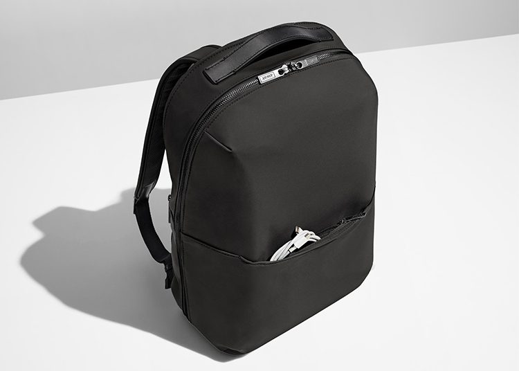 A sleek black backpack with a front pocket for earphones sits on a white surface, ready to complement any wardrobe.