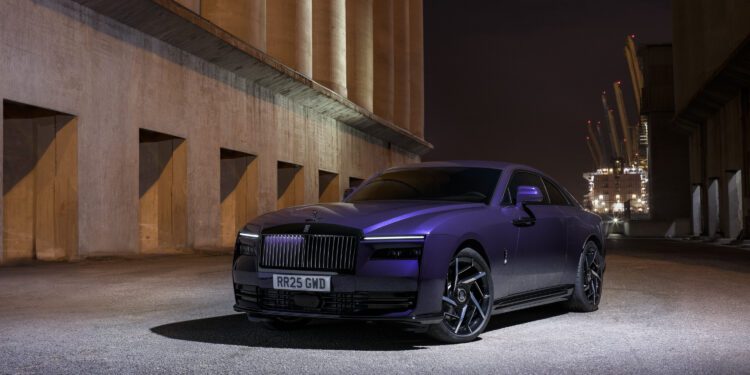 A purple luxury car is parked in a dimly lit industrial area at night.