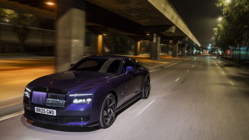 A purple luxury car drives on an empty city street at night.