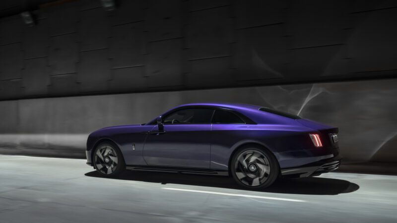 A sleek, dark purple luxury car drives quickly through a dimly lit tunnel.