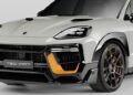 White SUV with a sporty design, showcasing a black and orange front bumper, sleek headlights, and a TECHART badge on the grille. This model exudes the prowess of the Porsche Cayenne MAGNUM edition.