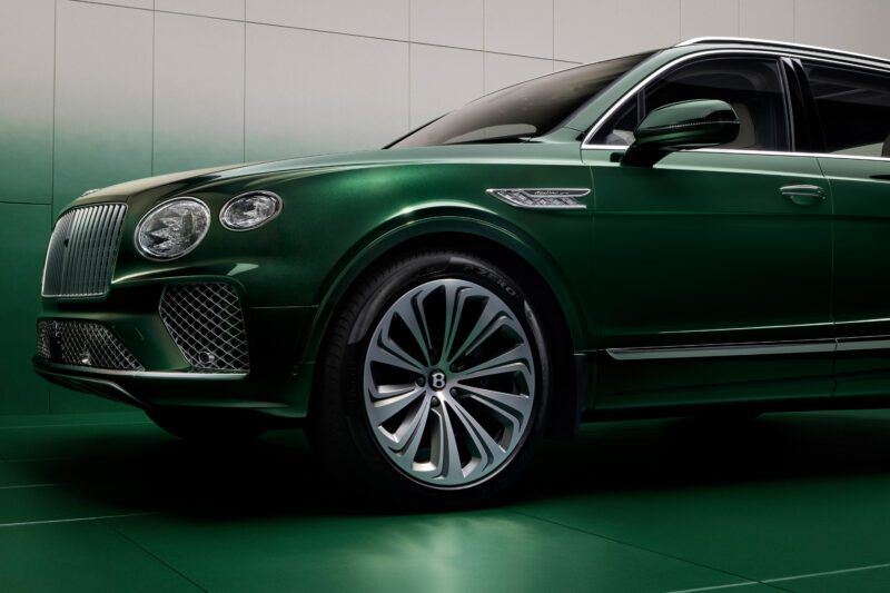 Green luxury SUV with intricate grille design, chrome accents, and distinctive alloy wheels, parked indoors on a green floor.